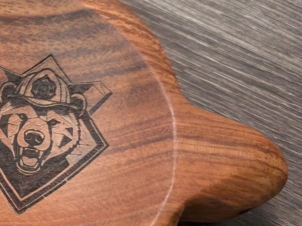 A bear in a firefighter's helmet, laser-engraved into a curved acacia board